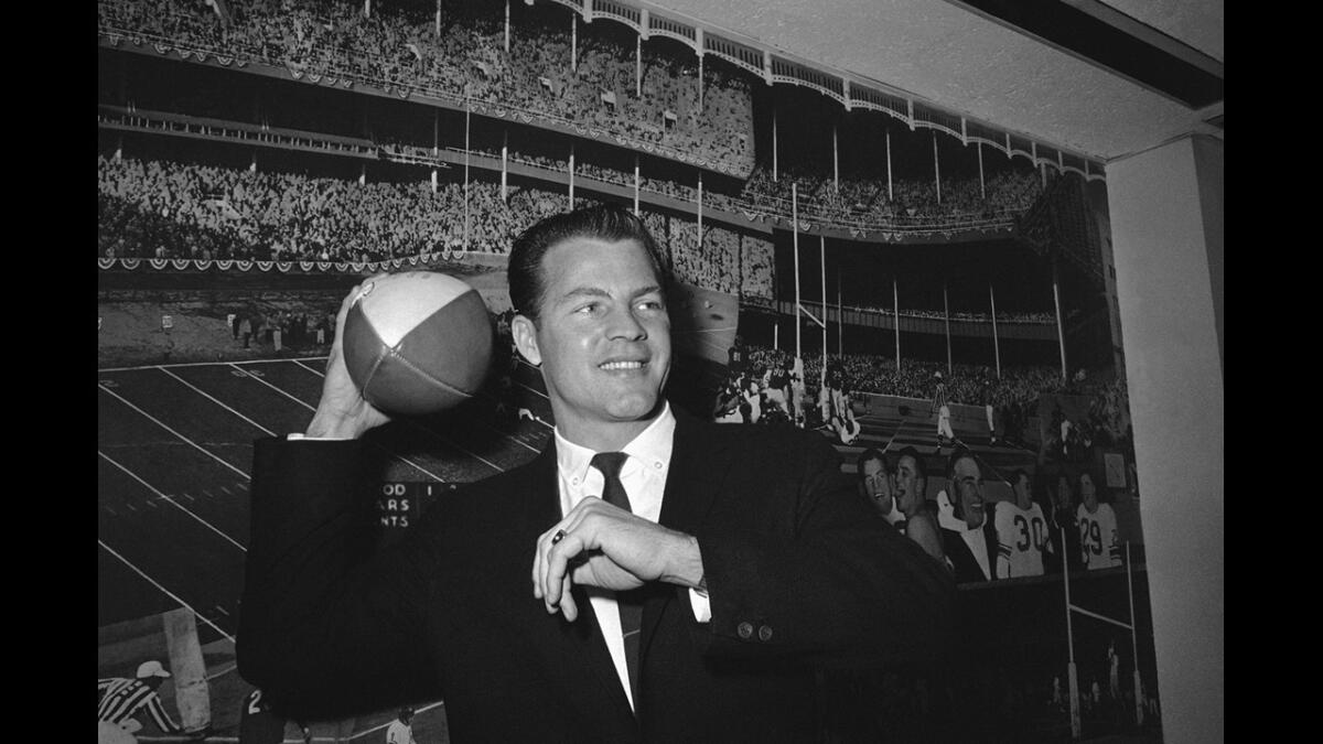 Halfback Frank Gifford cocks his passing arm as he stands in front of a photo mural of the Polo Grounds at the offices of the New York Giants in New York's Coliseum on April 2, 1962.