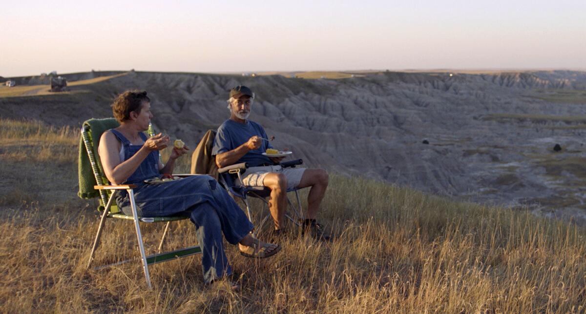 Frances McDormand and David Strathairn sit in a field in a scene from the film 'Nomadland'