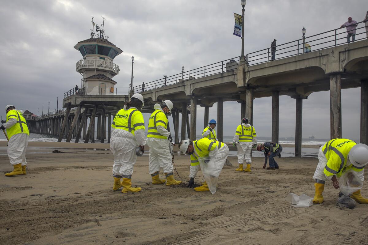 Workers remove oil from sand next to a pier