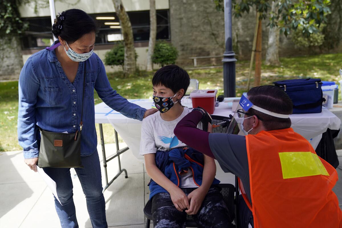 A woman rests her hands on a boy's shoulder as a health worker gives him a shot in the upper arm.