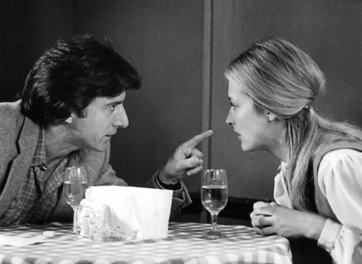 A black-and-white photo of a couple at a restaurant table, the man pointing his finger at the woman's face