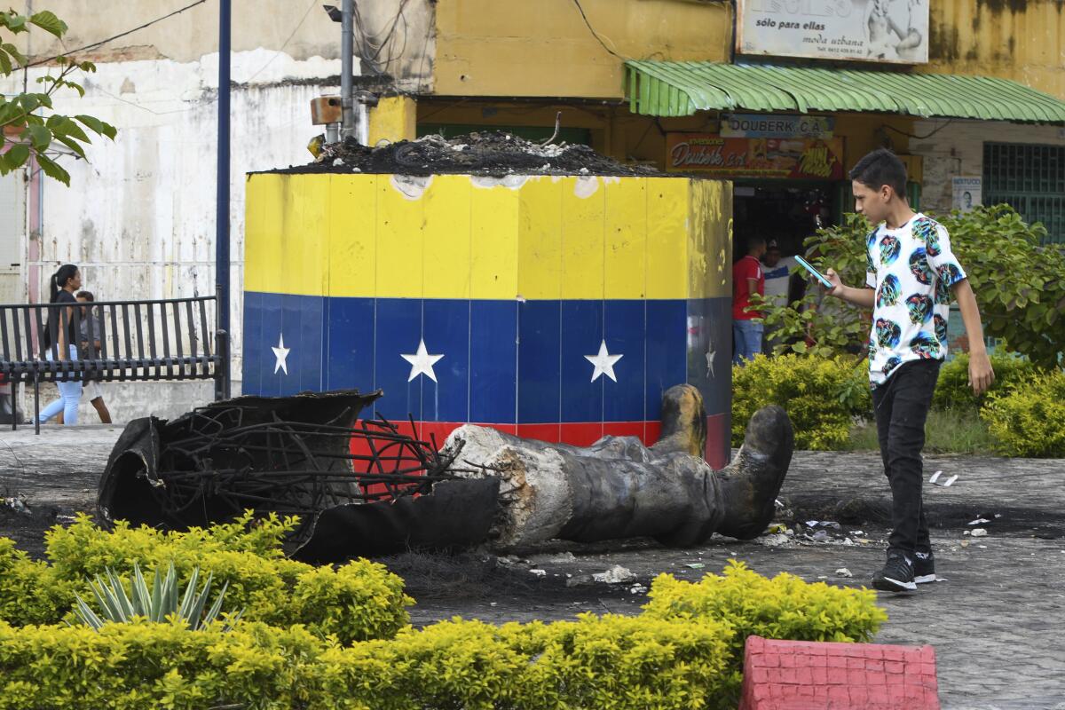 Una estatua destruida del fallecido presidente venezolano Hugo Chávez se encuentra junto a su base en Valencia