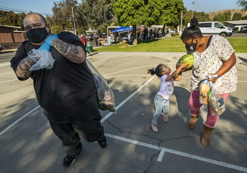 Michael Villalobos carries over his shoulder a bag with food. Kameo Allen, with a child, carries bread, a watermelon.