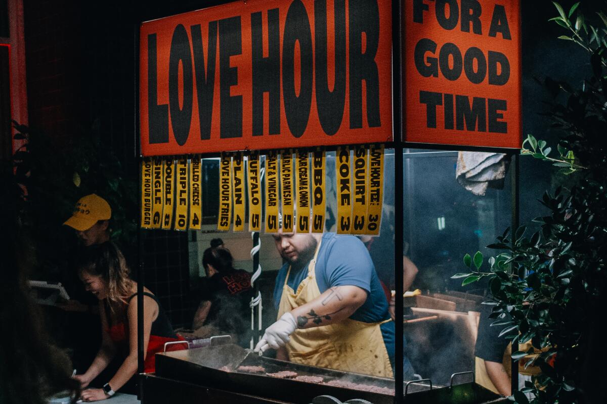 A chef flips burgers on the grill at Love Hour's Coachella pop-up