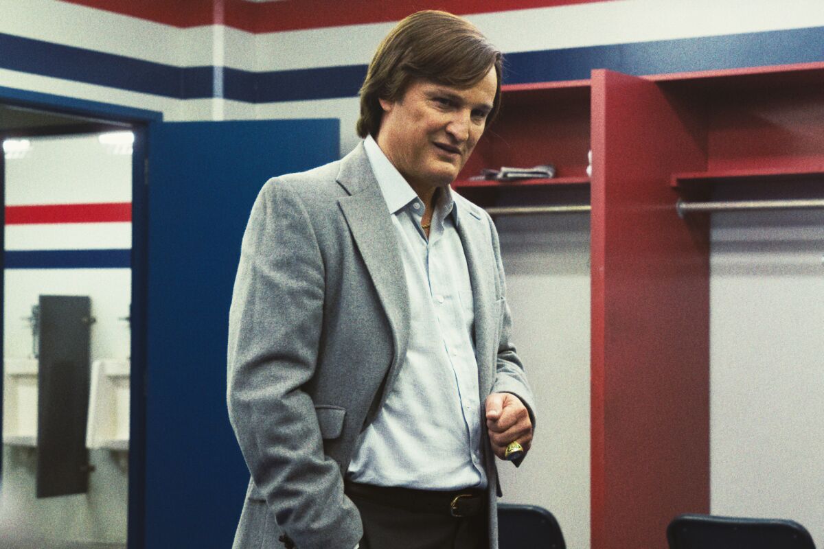 A man in a gray blazer stands in a locker room