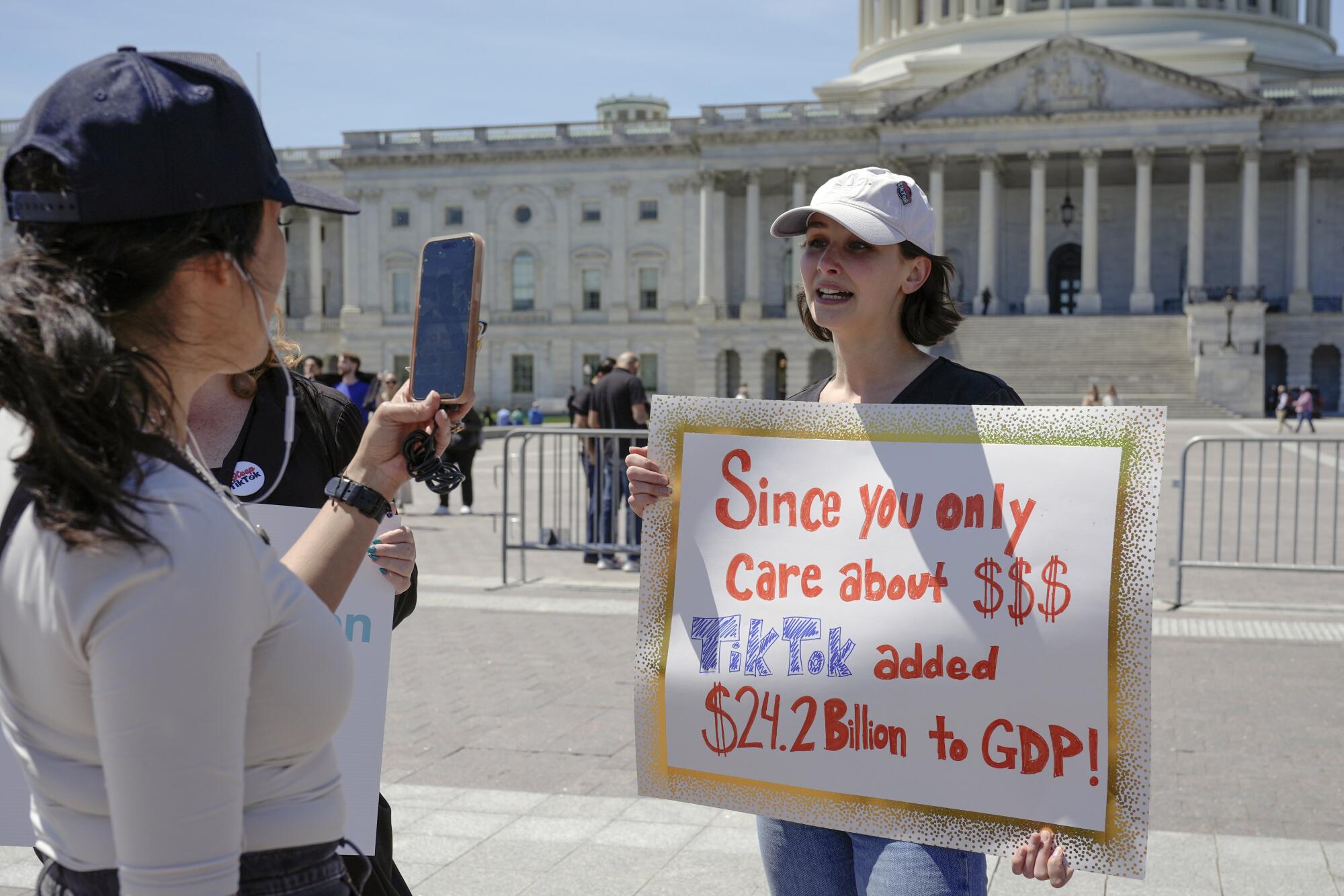 A reporter, left, pointing a smartphone to a TikTok creator holding a sign with the U.S. Capitol in the background
