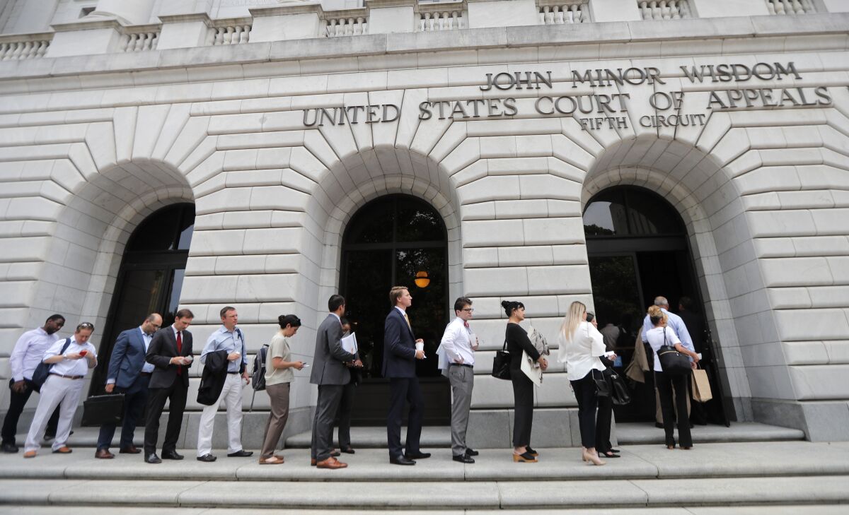 FILE - In this Tuesday, July 9, 2019 file photo, People wait in line to enter the 5th Circuit Court of Appeals to sit in overflow rooms to hear arguments in New Orleans. President Joe Biden's requirement that all federal employees be vaccinated against COVID-19 is awaiting judgment from a federal appeals court after arguments in New Orleans. An administration attorney told the court Tuesday, March 8, 2022, that a federal judge in Texas overstepped his authority when he blocked the mandate. (AP Photo/Gerald Herbert, File)
