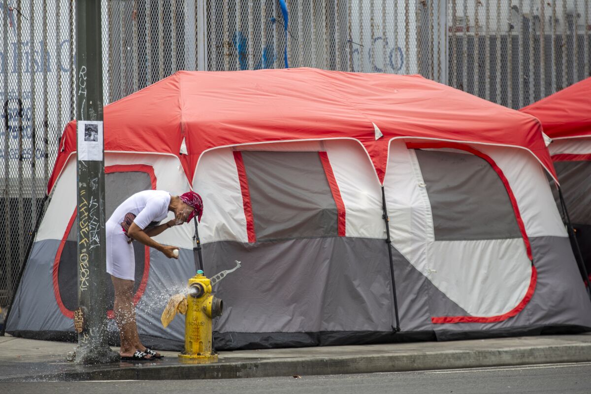 A woman stands beside a tent and an open water hydrant.