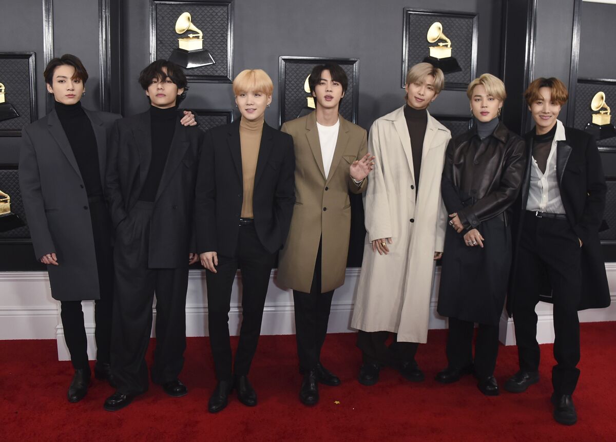 Seven fashionably dressed young men pose for a photo on a red carpet.