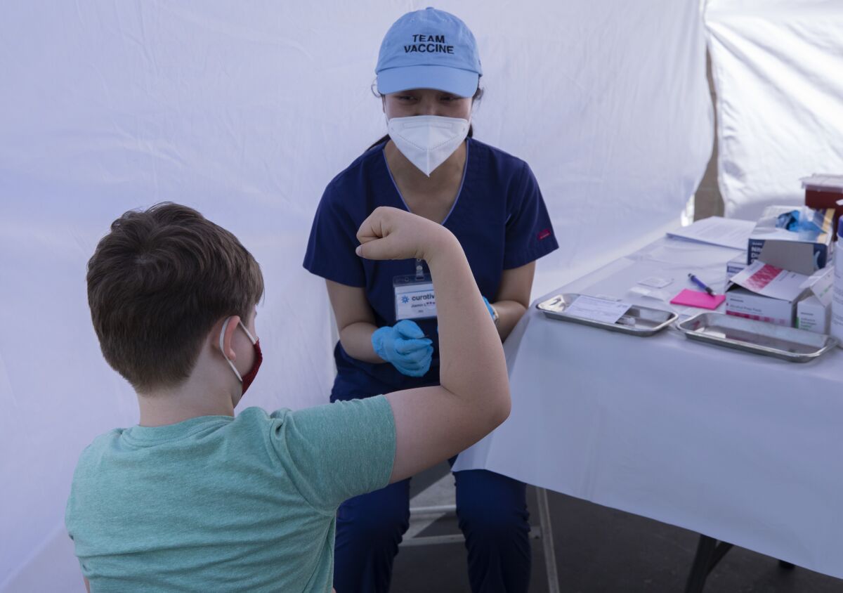 A boy flexes his arm as a nurse prepares to press a needle-less syringe against his arm.