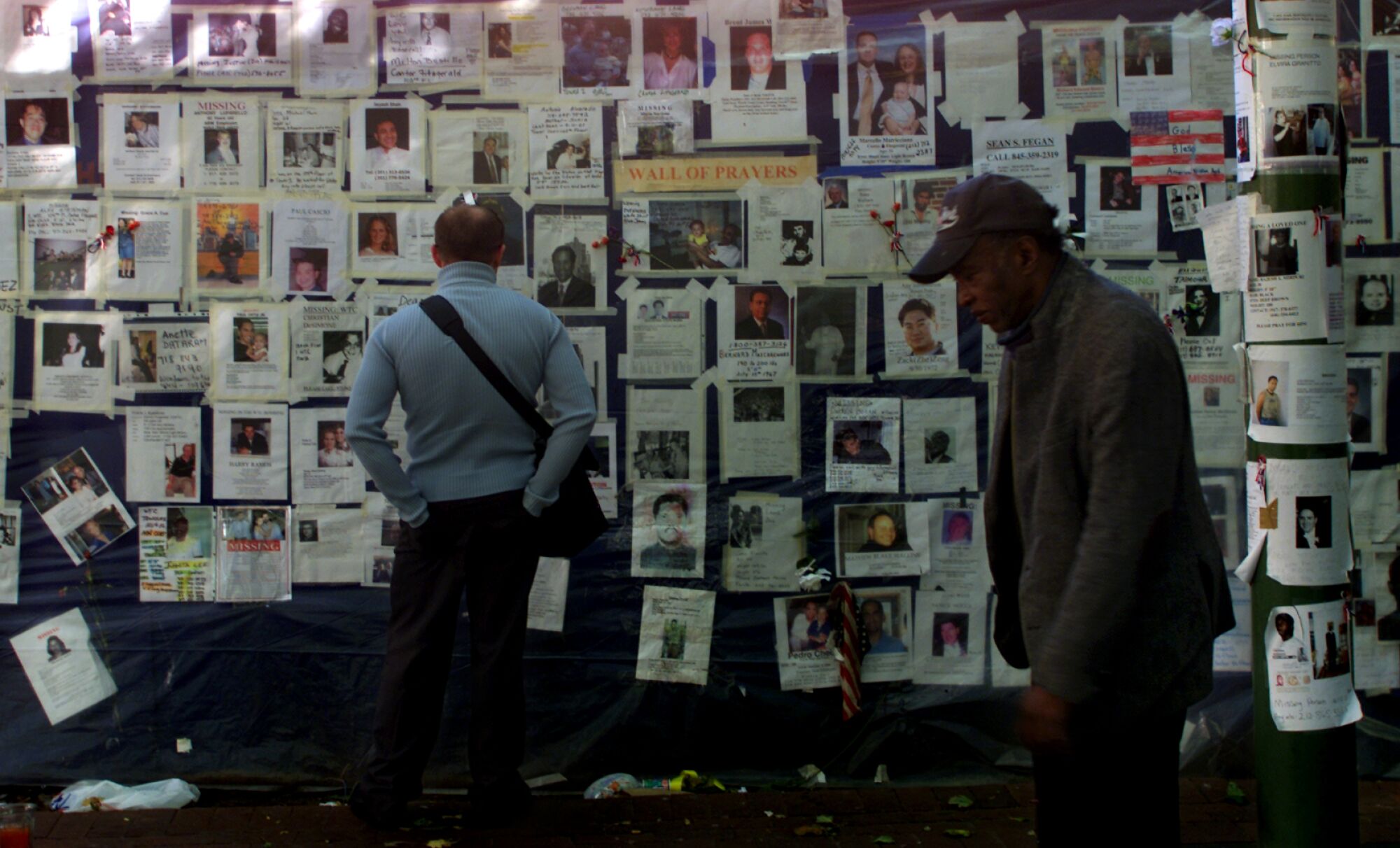 A man looks at missing-persons posters as another man walks past