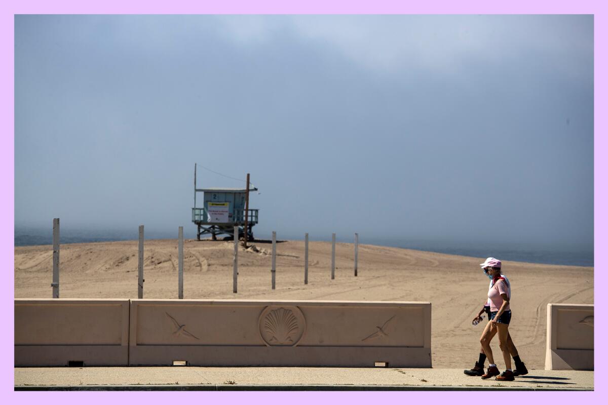 A couple walks along a stretch of beach with a lifeguard tower in the background.