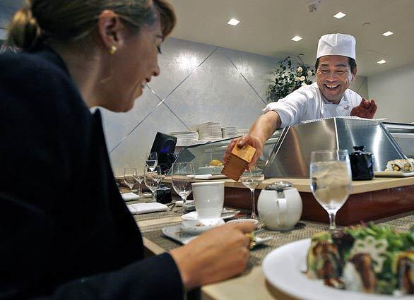 Sushi Chef Aki Yoshioka pours saki for Eileen Sanchez at the new Chaya Downtown restaurant in downtown L.A.