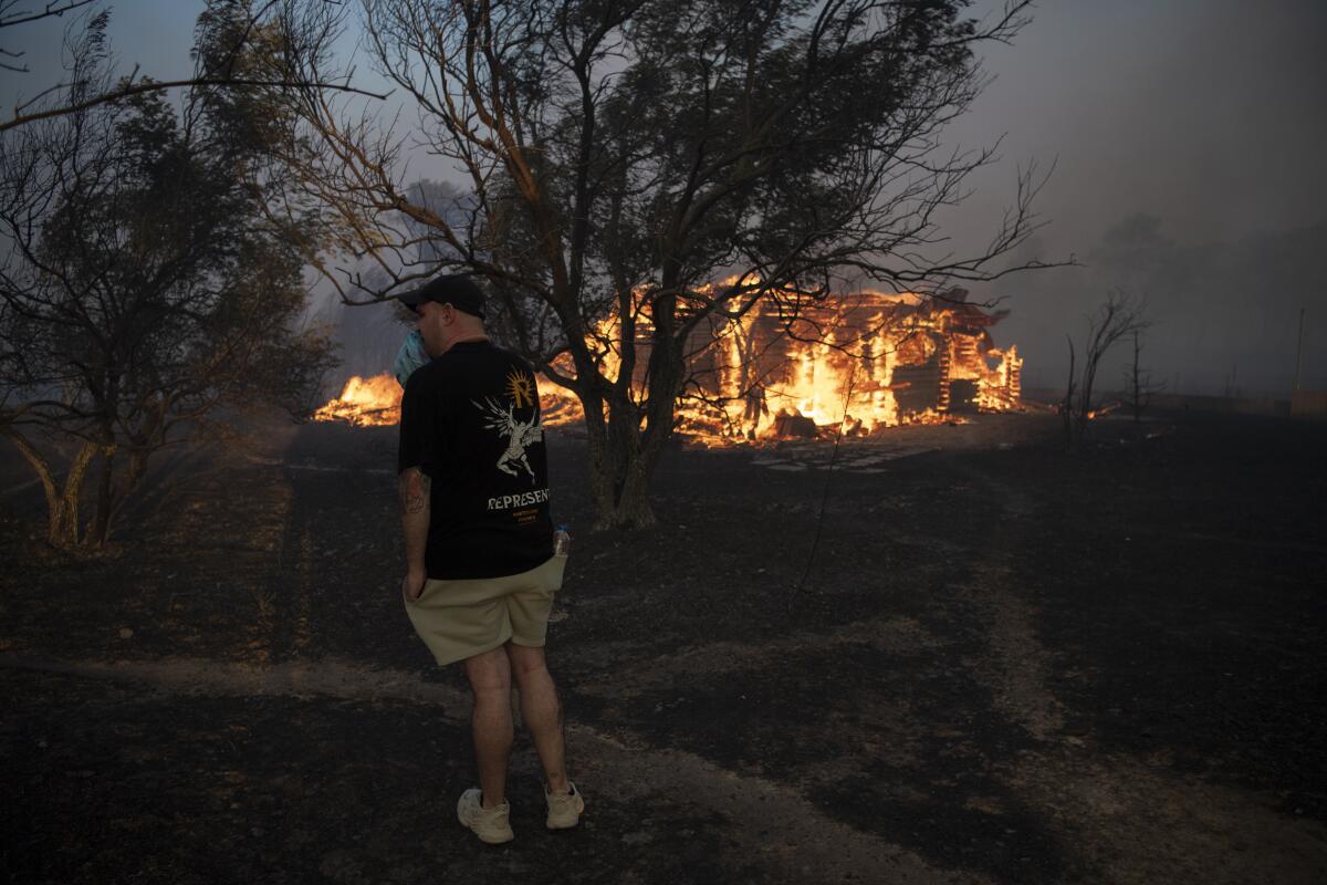 A house is on fire as a man watches from a distance behind trees