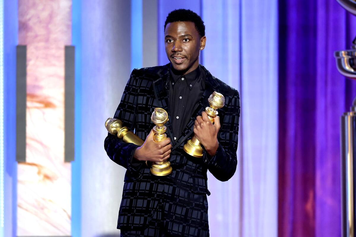 A man in a plaid suit holds three Golden Globes.