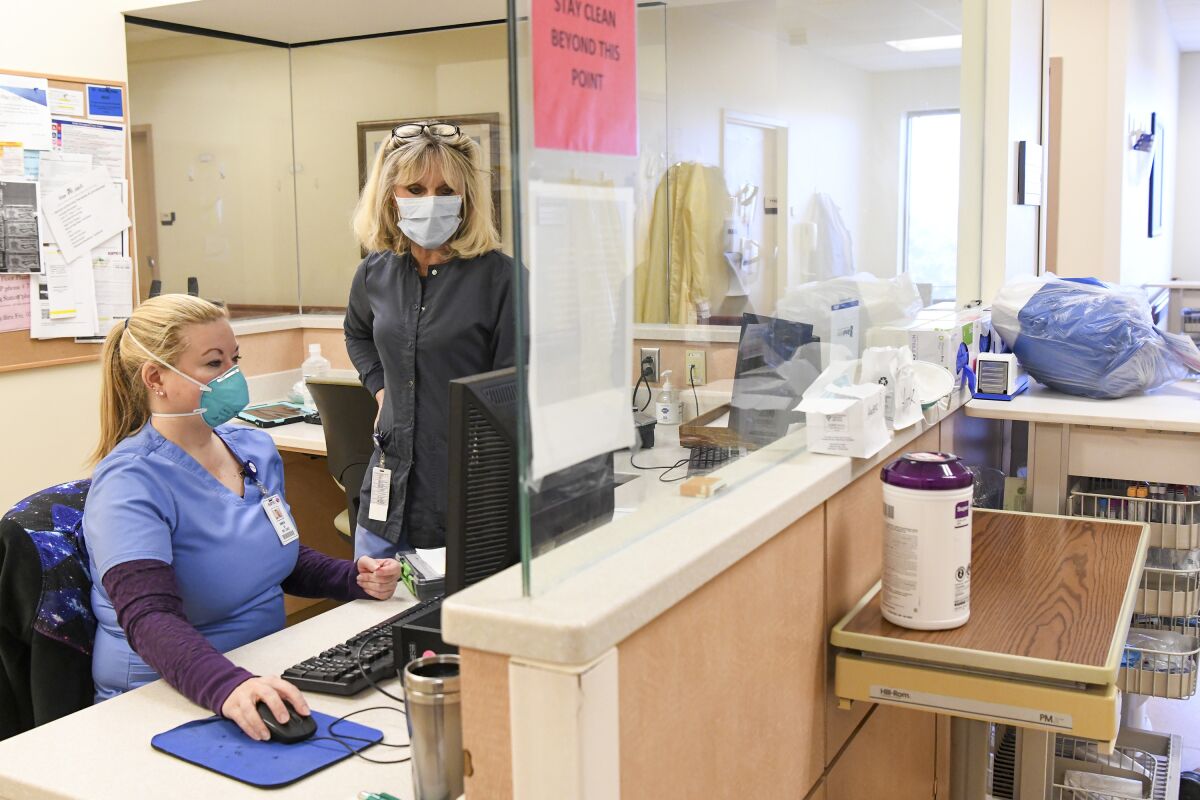 Two women in scrubs and masks look at a computer monitor inside a hospital.