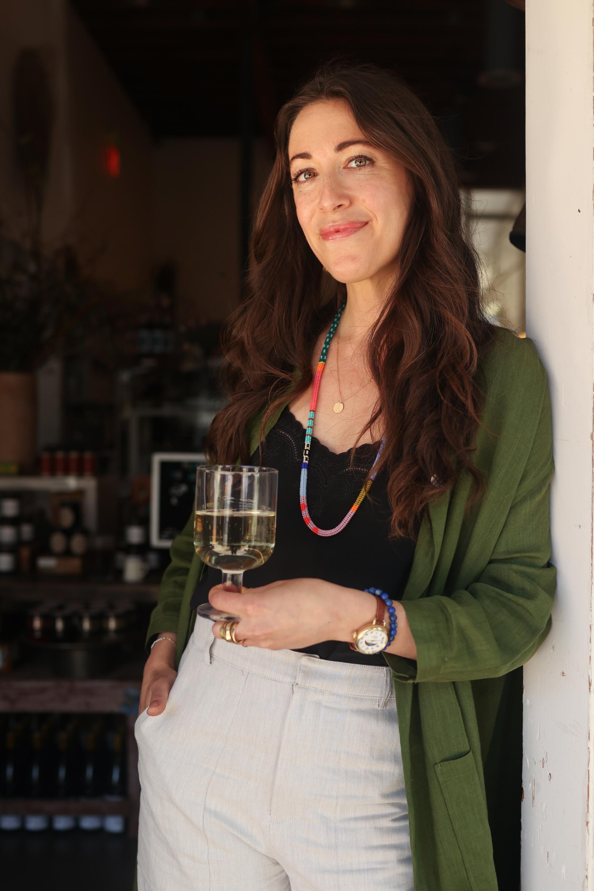Botanica co-owner Heather Sperling lean against a wall, holding a glass of wine, at her restaurant
