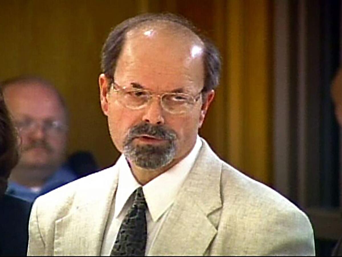 A balding man in a beige suit rolls his eyes.