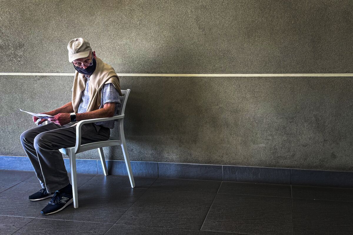 A masked man sits in a chair holding paperwork and waits to pay for a coronavirus test.