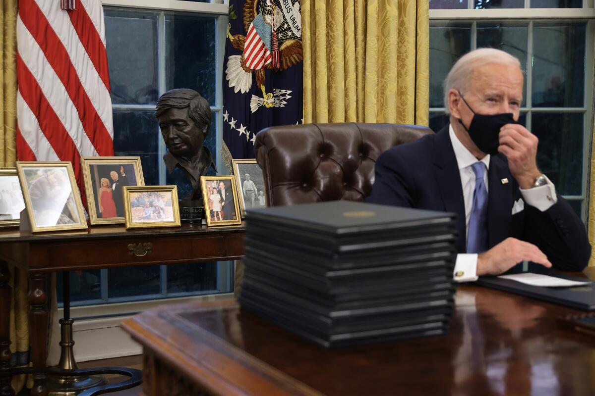 A sculpted bust of Cesar Chavez is displayed on a table behind President Biden 