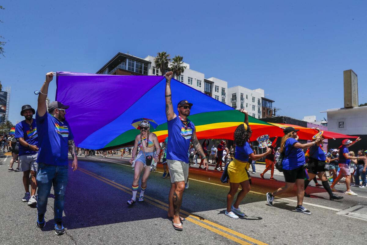 Marchers carry a large rainbow flag down a street on a sunny day 