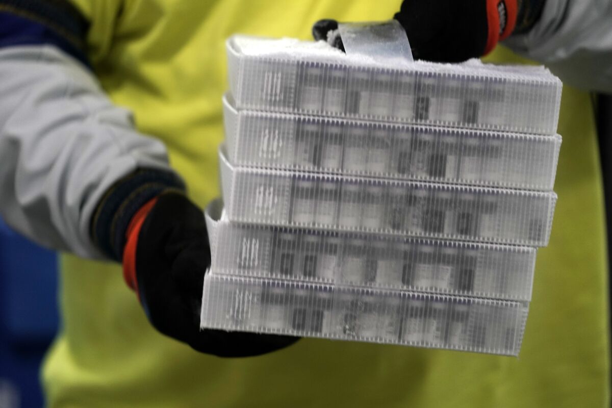 A worker wearing gloves holds small boxes containing vaccine, which are kept in cold storage.