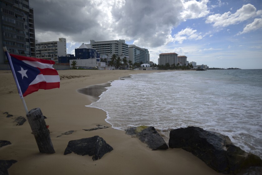 FILE - In this May 21, 2020 file photo, a Puerto Rican flag flies on an empty beach at Ocean Park, in San Juan, Puerto Rico. The number of tourists arrested in Puerto Rico on charges of violating COVID-19 measures is increasing as the U.S. territory cracks down on visitors who stay out past curfew and refuse to wear face masks or remain under quarantine, authorities said Tuesday, March 23, 2021. (AP Photo/Carlos Giusti, File)