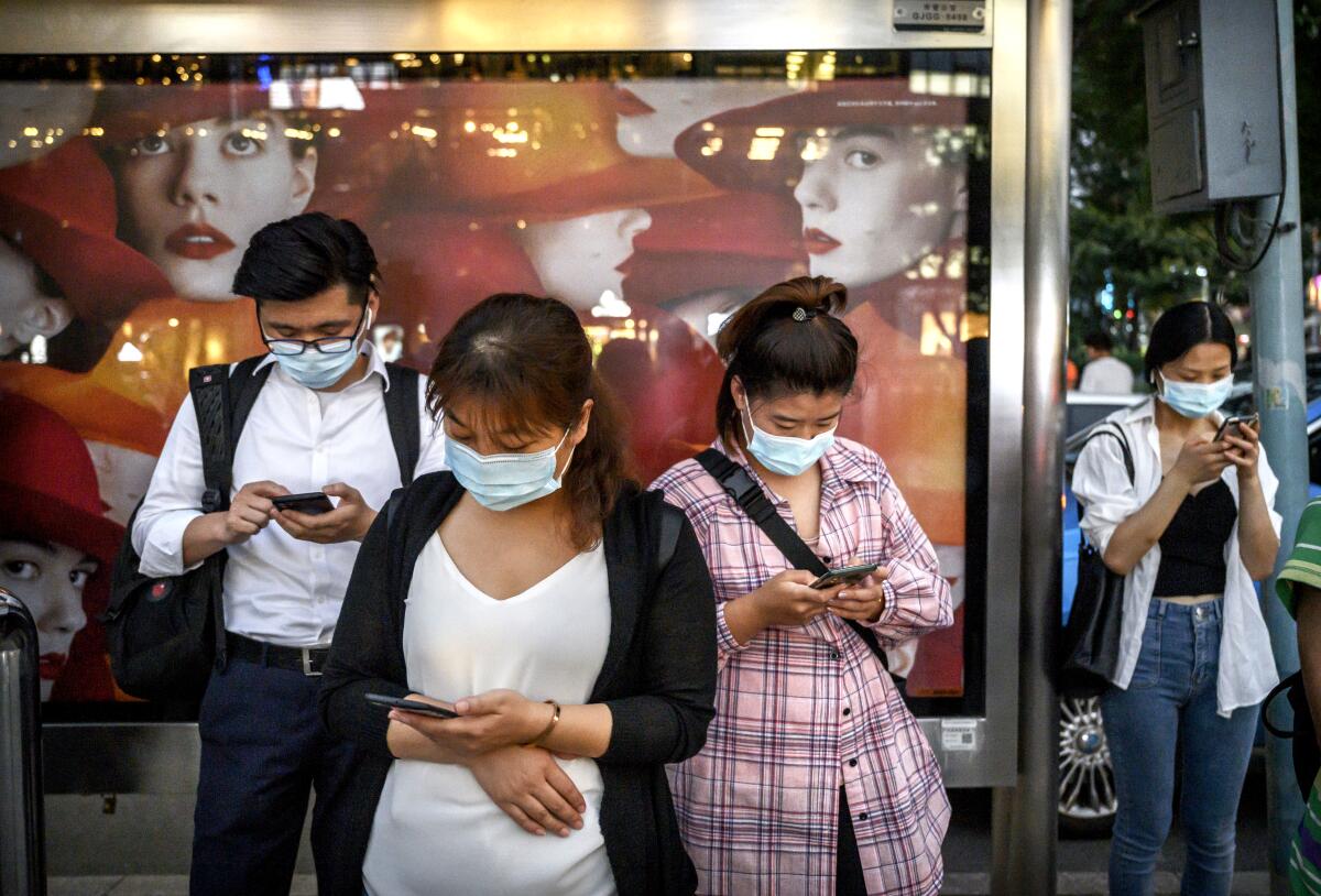 Masked people waiting at a bus stop look at their cellphones 