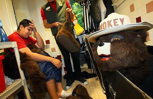 Andrew Garza, 16, a high school senior from Santa Ana, wipes his brow after a session dressed as Smokey Bear at the Discovery Science Center in Santa Ana. Helping Garza pack up the bulky suit is Juan Plascencia, who guides him in crowds because of the costume's limited visibility.
