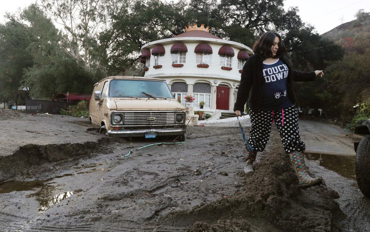 A woman trudges through mud piled on La Tuna Canyon Road after checking on her neighbor whose house was blocked by a mudslide that struck the area.