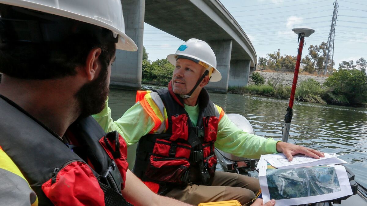 Caltrans bridge engineer Kevin Flora, right, and student assistant Rami Gharaibeh float up the San Gabriel River to inspect the foundations of the pillars supporting the 405 Freeway span over the waterway.