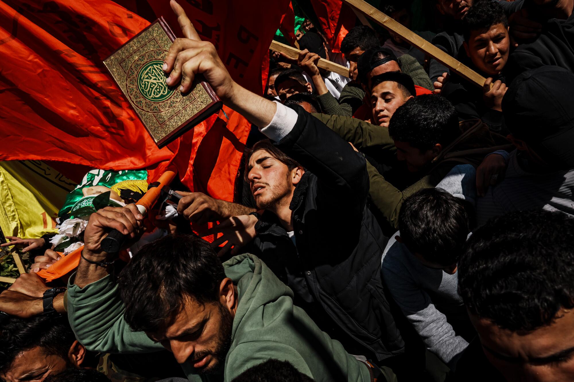 A man holds the Quran while joining other community members and relatives carrying the body of Amro Najjar.
