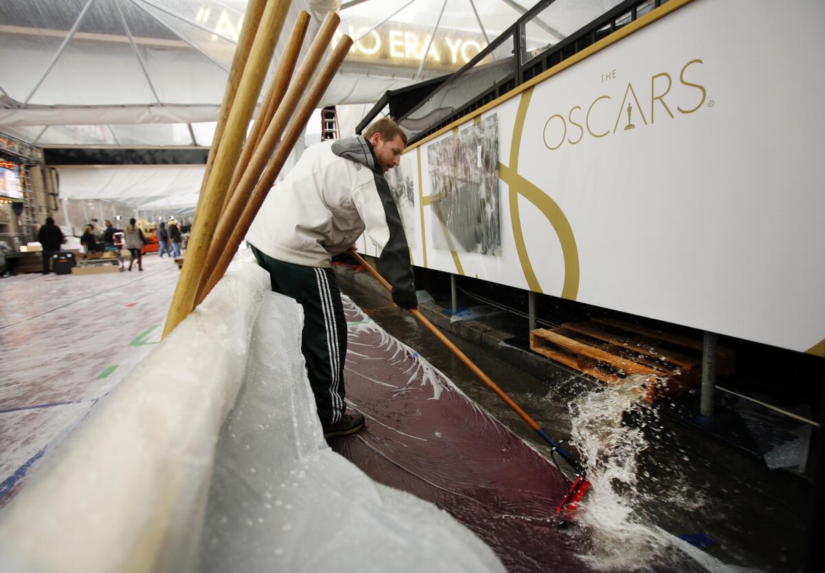 Jon Rosenberg, uses a squeegee to push running water off the red carpet under tents on Hollywood Blvd as rain pours outside the Dolby Theater at Hollywood and Highland on February 28, 2014 as rehearsals and preparations continue for the Oscars which will be on this Sunday March 2. ( Al Seib / Los Angeles Times )