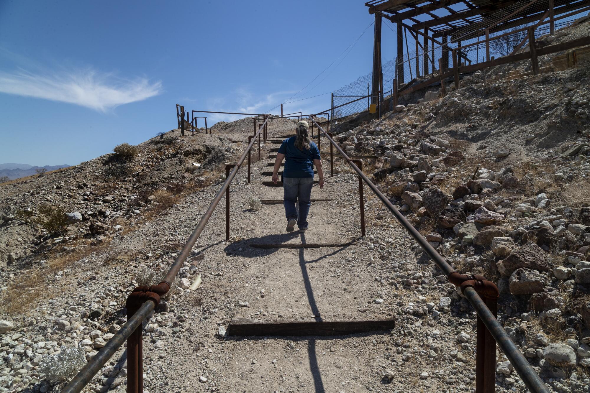 A woman walks up a dirt path between metal railings.