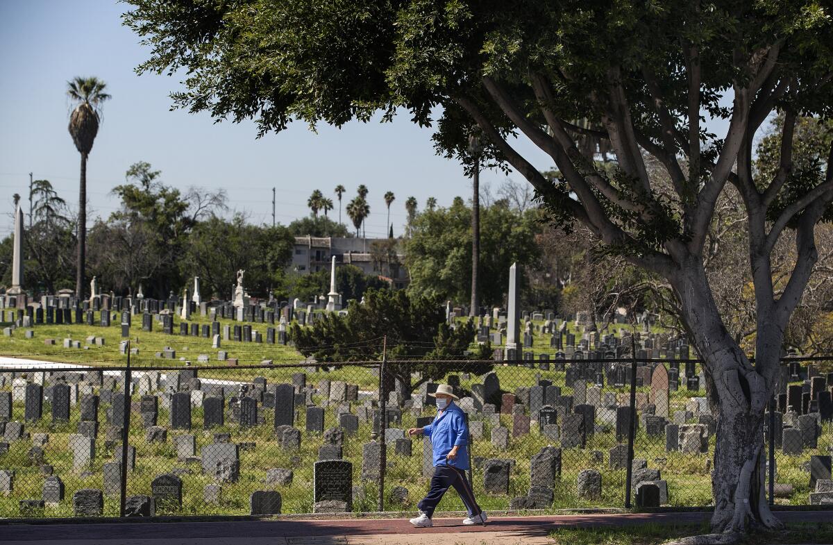 A man walks along Cesar Chavez Avenue in Boyle Heights with Evergreen Cemetery, seen in the background. 