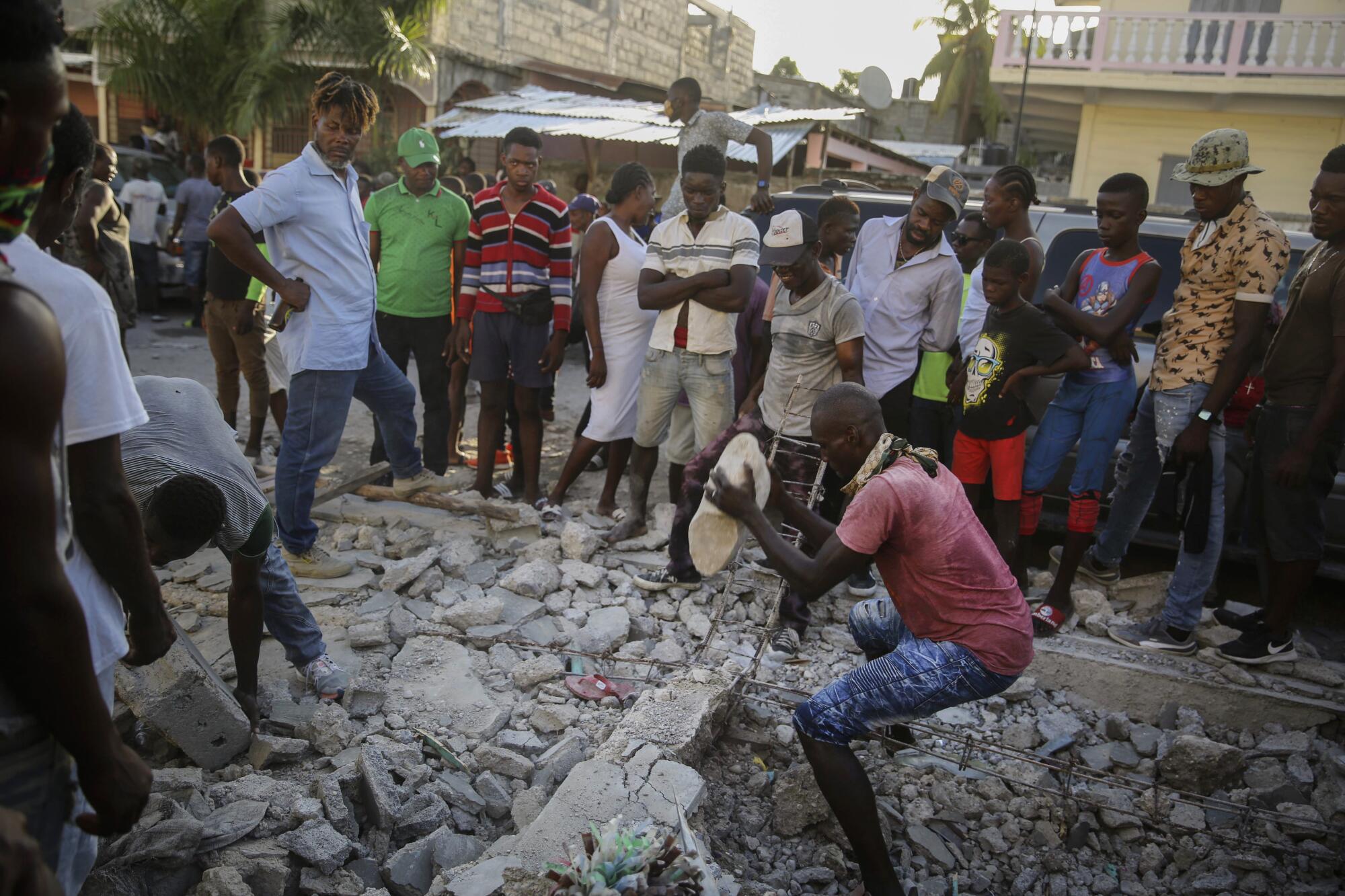 A man digs with a stone through the rubble of a house destroyed by an earthquake while onlookers watch