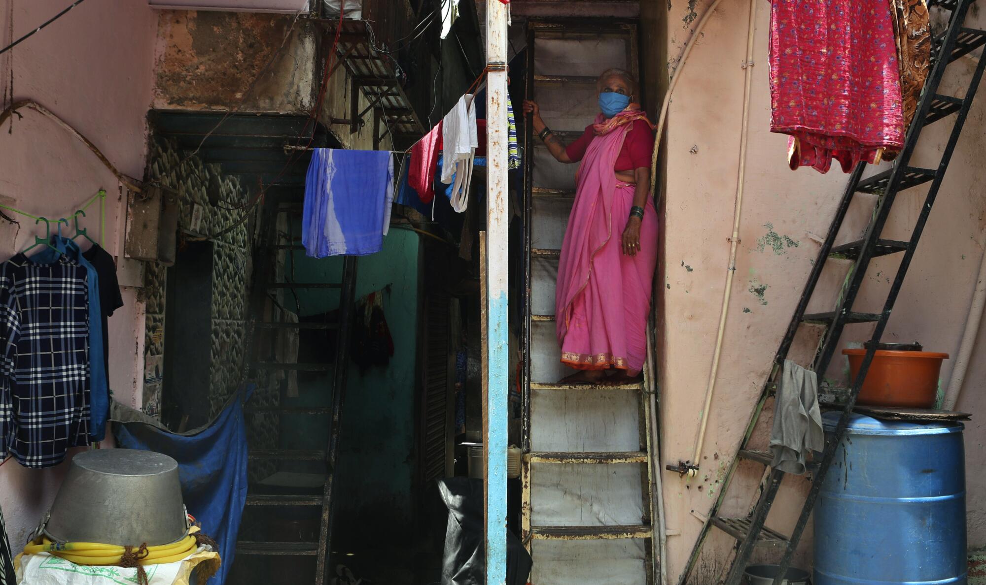 A woman wearing a mask stands on her staircase in Dharavi.