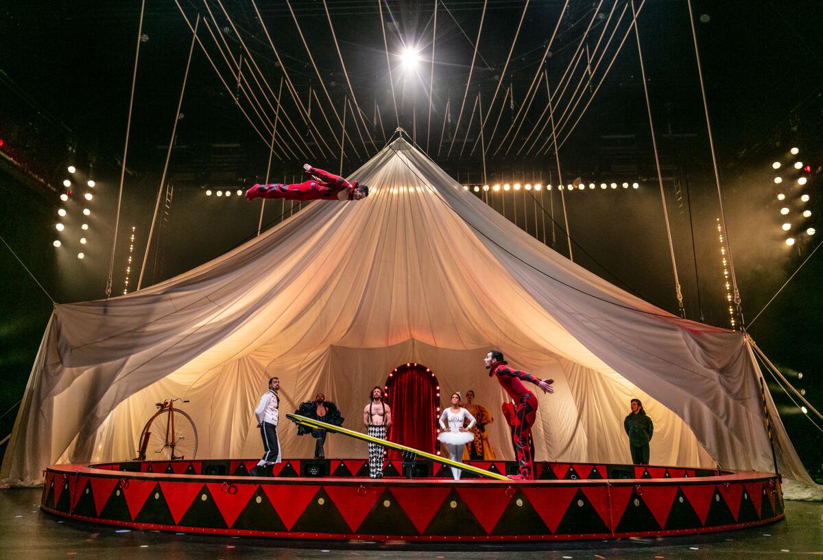 People stand under a tent looking up at a man in the air