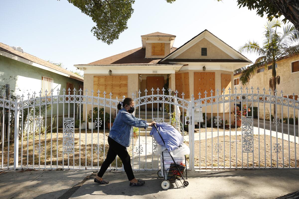 A woman walks past a boarded-up home.