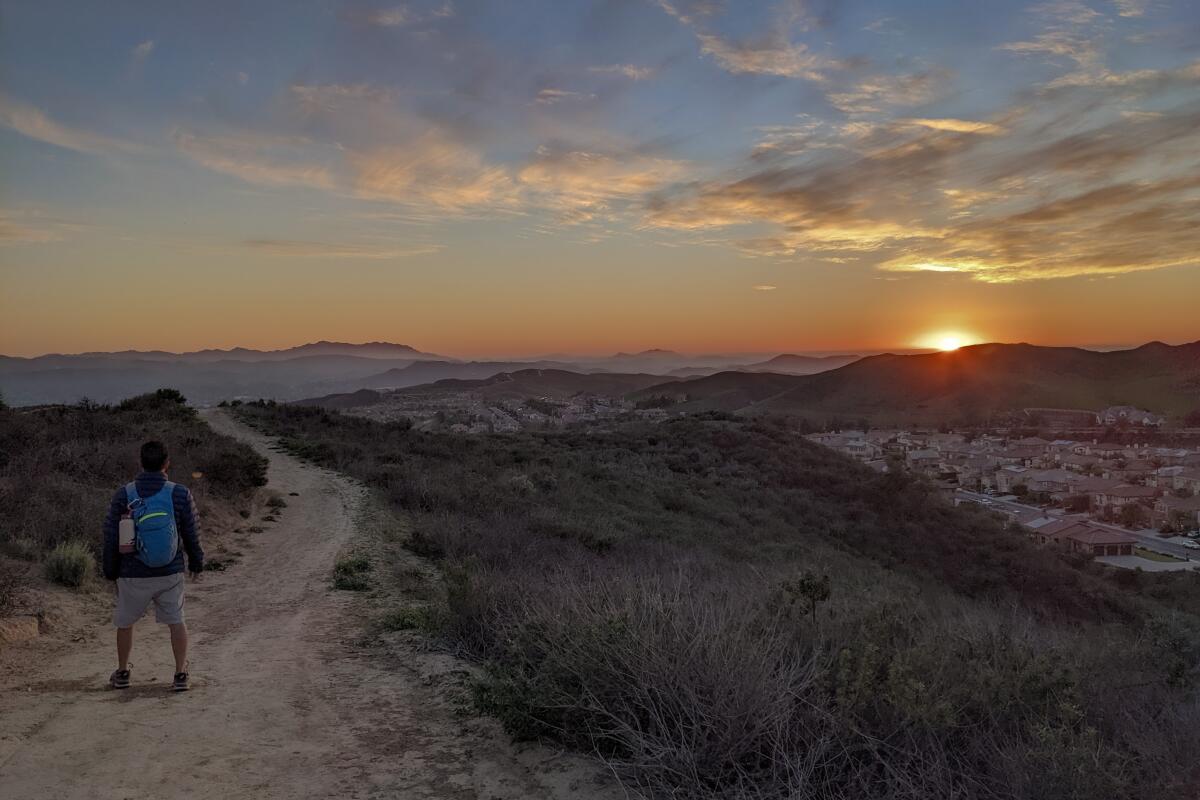 A hiker on the dirt path of Big Sky Trail at sunset. 