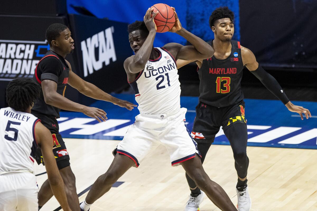 Connecticut's Adama Sanogo controls the ball between Maryland's Darryl Morsell and Hakim Hart.