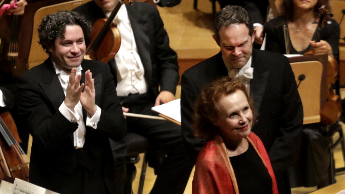 Composer Kaija Saariaho stands with Gustavo Dudamel and baritone Gerald Finley applauding behind her.
