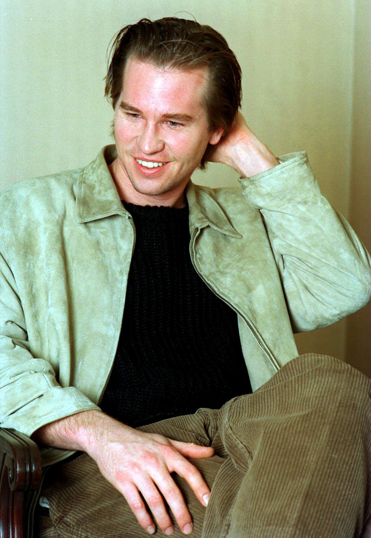 A man in a light green shirt runs his hand through his hair and smiles.