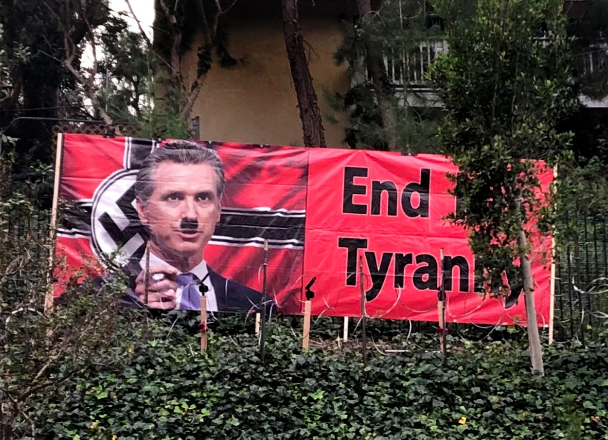 A banner with an image of Gavin Newsom altered with a Hitler mustache, in front of a Nazi flag next to the words End Tyranny