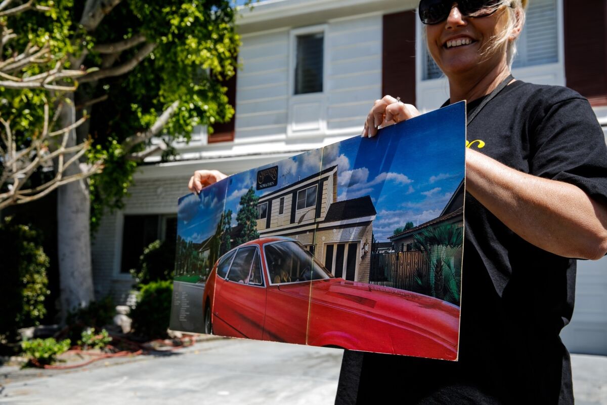 Toni Lee from England holds up the "Now & Then" album art that features the Carpenters' Downey, Calif., home, as she stands in front of the house on April 25, 2019.