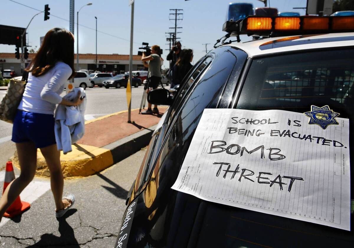 A Cal State L.A. student runs past a sign taped on a law enforcement vehicle that reads "School is being evacuated. BOMB THREAT." School administrators ordered the campus cleared, but many students said directions were not clear and chaos ensued.