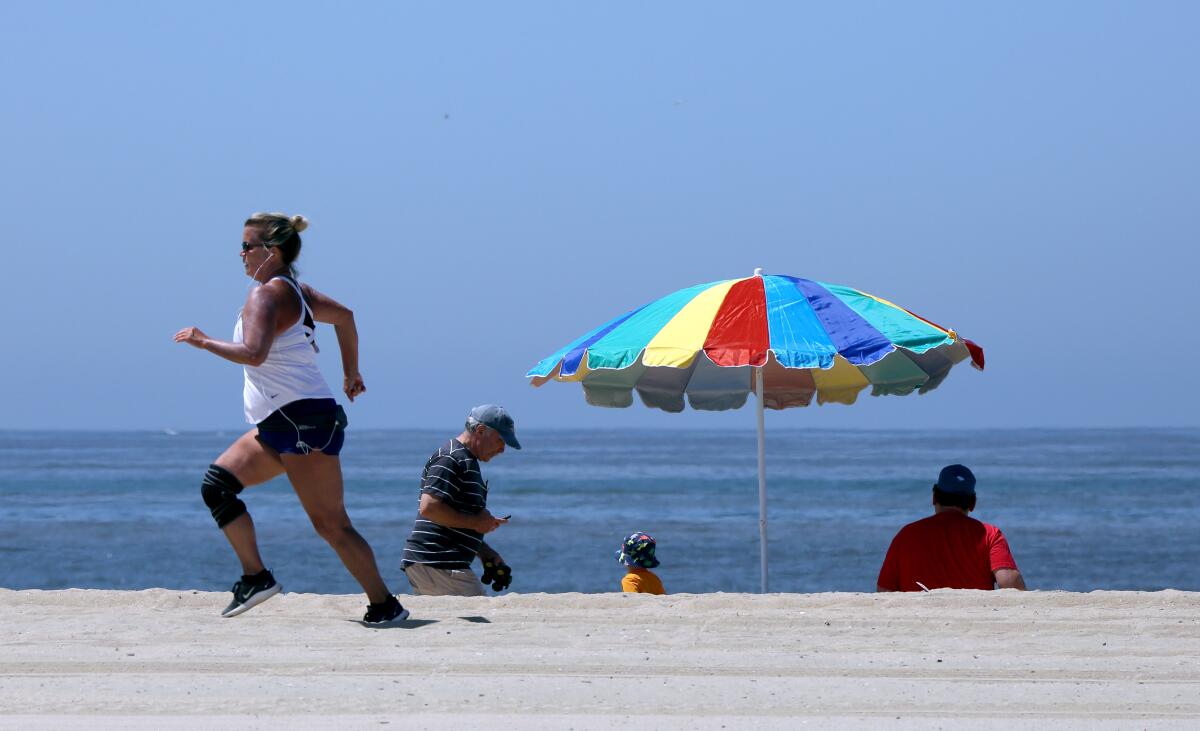 A woman runs on the sand as others take in the sights on the beach next to the Balboa Pier in Newport Beach on Wednesday. The city partially opened its beaches under an "active recreational use" plan approved today by state officials.