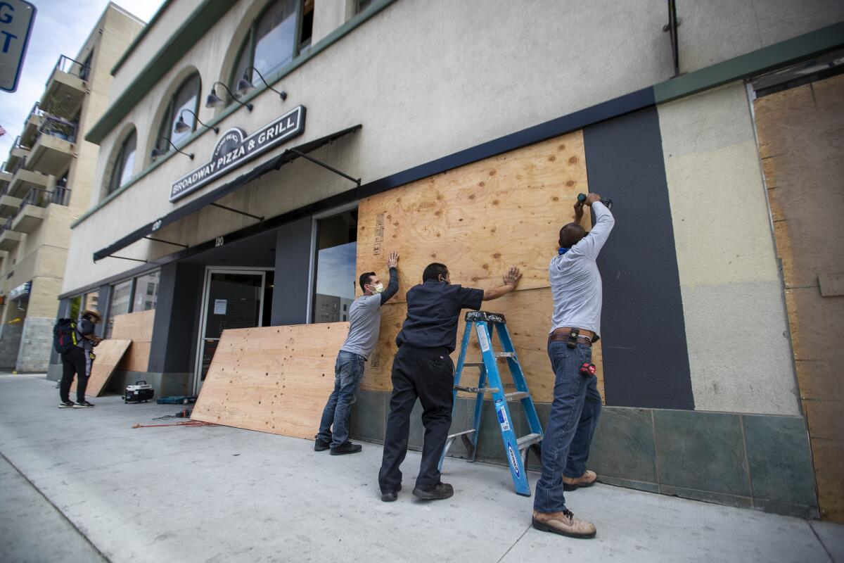 Workers put plywood over windows along Pine Avenue in Long Beach on Monday.