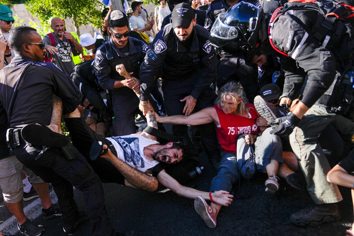 İsrail polisi göstericileri dağıtırken bir erkek ve bir kadın birbirine tutunmaya çalışırken bağırıyor.