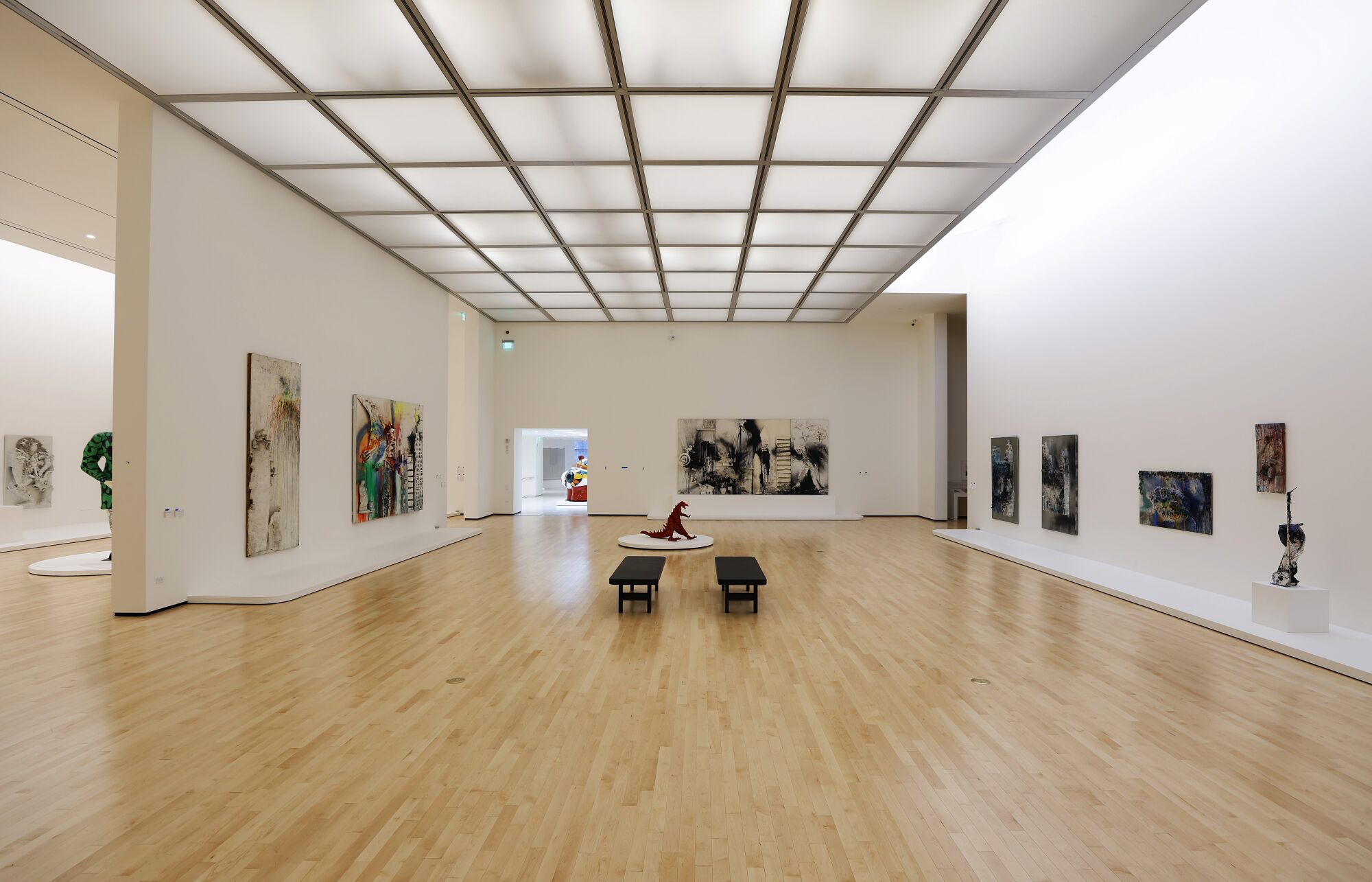 An art gallery with two benches, a dinosaur sculpture on the floor and paintings on the walls